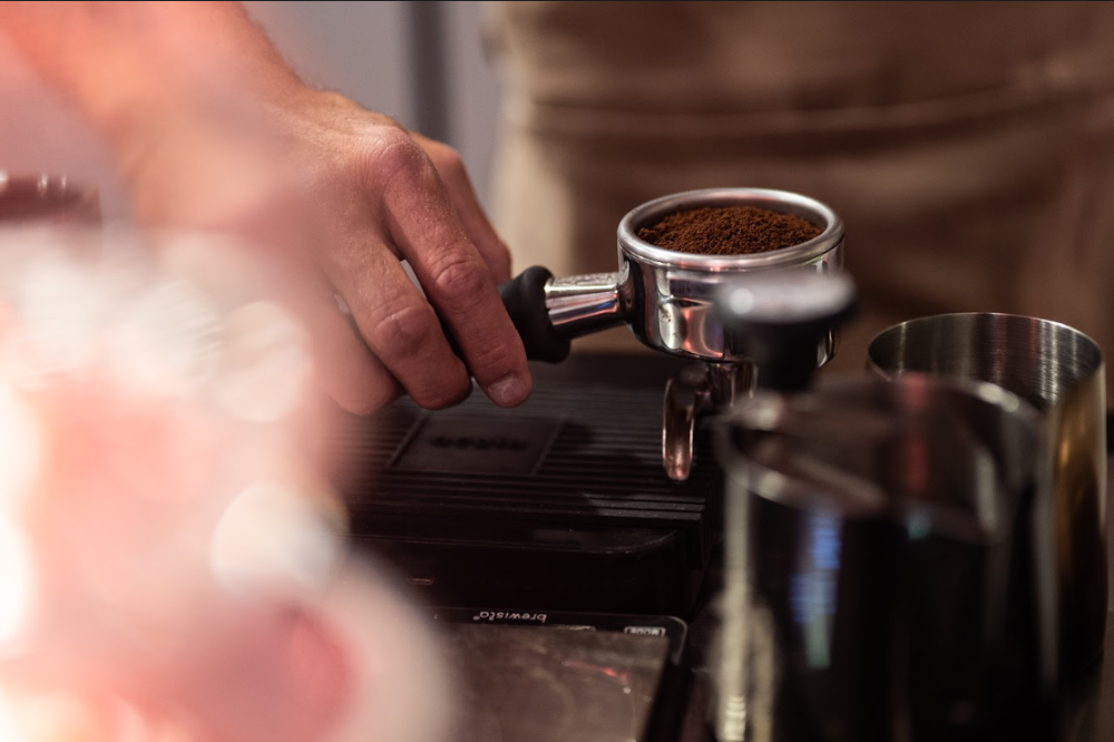 Barista przygotowujący espresso na profesjonalnym ekspresie, zbliżenie na ręce przy pracy za barem kawiarni